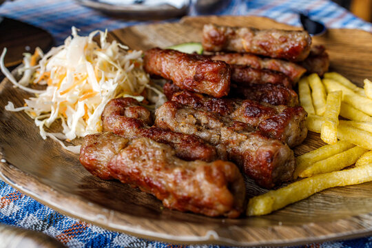 Cevapi served on a wooden plate with sides of fries and cabbage salad at a local eatery