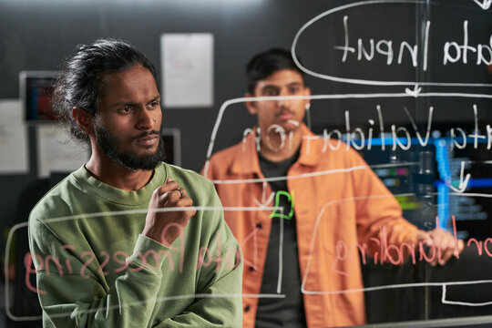 Men planning software workflow on glass board, collaborating in tech office. Ideal for startup teamwork, coding, innovation, product development marketing