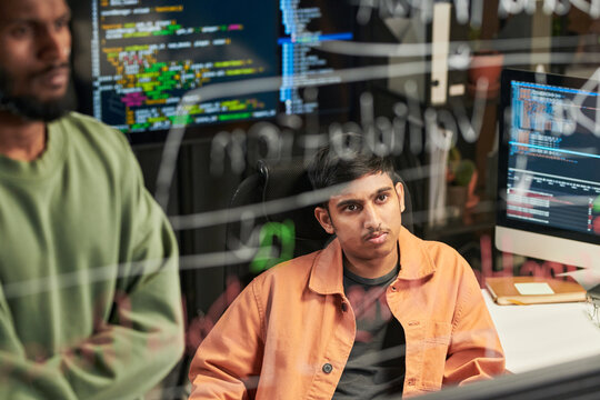 Young man analyzing code with colleague in software development office, discussing programming workflow. Useful for IT teamwork, coding, cybersecurity marketing