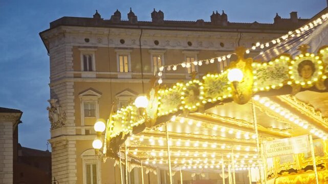 Beautiful merry-go-round with golden lights turning in an old european town square at twilight. Nostalgic amusement ride creating a magical atmosphere