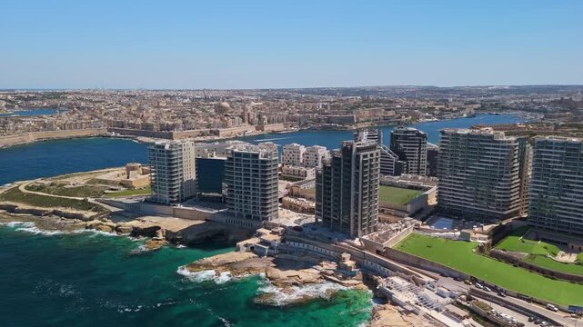 In Sliema, Malta, an aerial view captures the urban coastline with modern buildings and public spaces along the Mediterranean Sea and the waterfront near Tigne and Valletta.