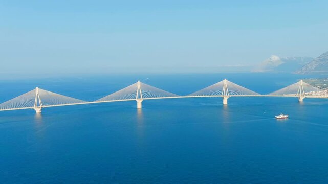 Patras, Greece. The Rio-Antirrio Bridge, a sweeping multi-span cable-stayed structure with four delta-shaped pylons spanning the deep blue Gulf of Corinth, Drone footage under clear summer sky. Drone