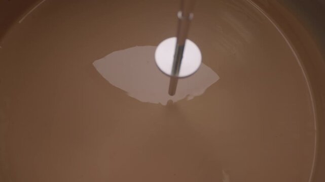 Top-down close-up of a brown liquid being stirred inside a container using a rod