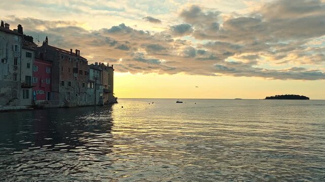 Warm sunset over Rovinj old town waterfront and calm Adriatic sea, golden video frame with historic homes, soft clouds, small island and water reflections