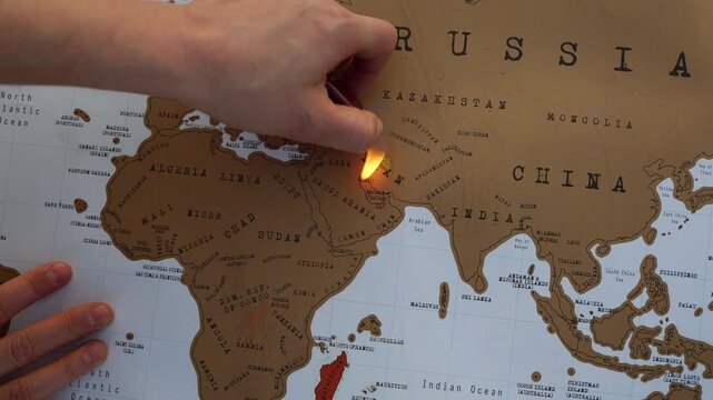 Hand holds a lighter flame over Iran on a world map symbolizing armed conflict geopolitical tensions war escalation and humanitarian crisis in the region