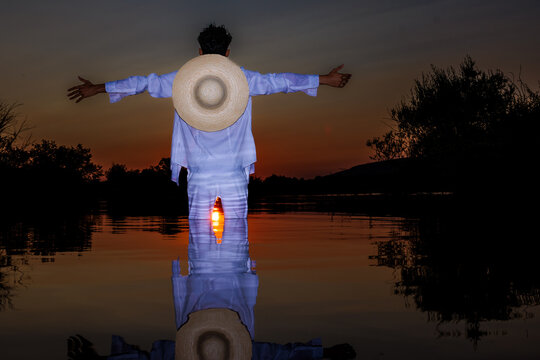 Man with straw hat and outstretched arms enjoying summer sunset on water