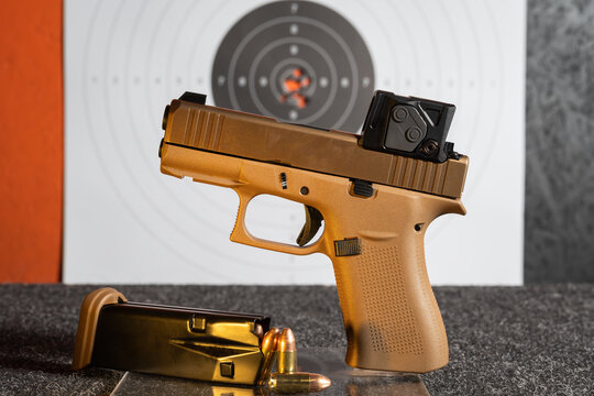 Modern semi automatic pistol with red dot sight and loaded magazine with 9mm bullets on shooting range table with target background