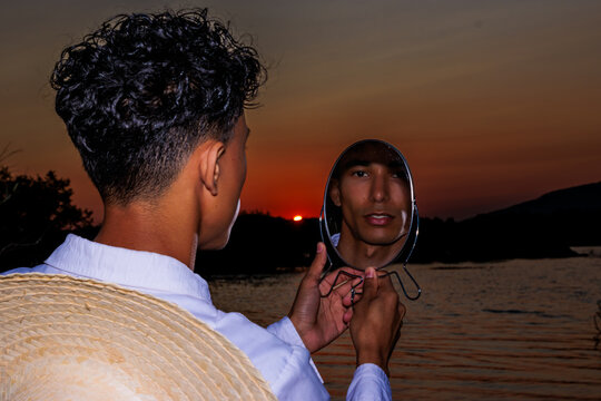 Young man holding mirror reflecting himself at sunset, contemplating identity and future