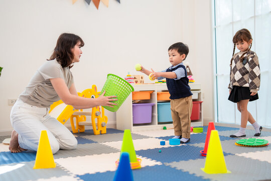 Children playing with toys and learning to sort objects in a classroom with a teacher guiding them