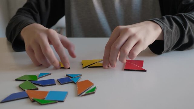 Focus on hands assembling geometric shapes. Young learner engaging with colorful puzzle pieces at desk. Educational environment with child assembling wooden puzzle pieces under natural light