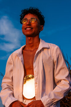 Young man reflecting summer sunset and freedom with mirror in white shirt