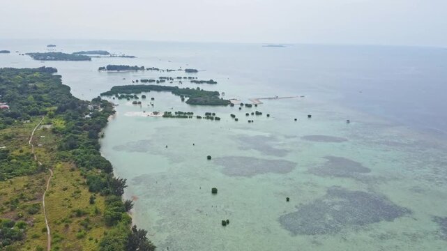 Aerial view of a tropical island archipelago surrounded by clear turquoise sea and coral reefs. Drone shot of an island strip with green trees in the ocean. Pari island in Indonesia 