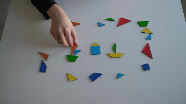 Vivid wooden blocks. Teen is arranging colorful geometric shapes. Overhead view of hand positioning shape blocks. Child engaging with vibrant wooden pieces to develop fine motor and pattern skills