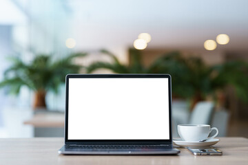 Obraz premium Mockup of laptop computer with empty screen with coffee cup and smartphone on table of the coffee shop background,White screen