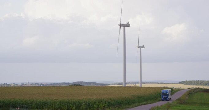 Blue truck driving on a country road passing wind turbines in a field