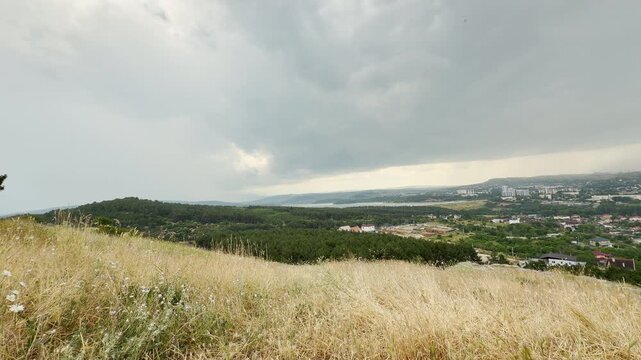 Dark storm clouds bring a refreshing summer shower over the landscape of Simferopol, Crimea. Dry grass fields wait quietly under the dramatic sky, bringing a peaceful sense of wonder.