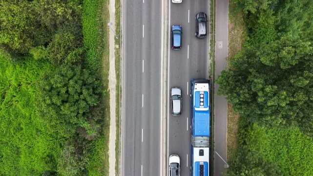 Aerial view of a traffic jam on a busy road, showcasing multiple vehicles including cars and a bus, surrounded by greenery and urban infrastructure in a vibrant setting