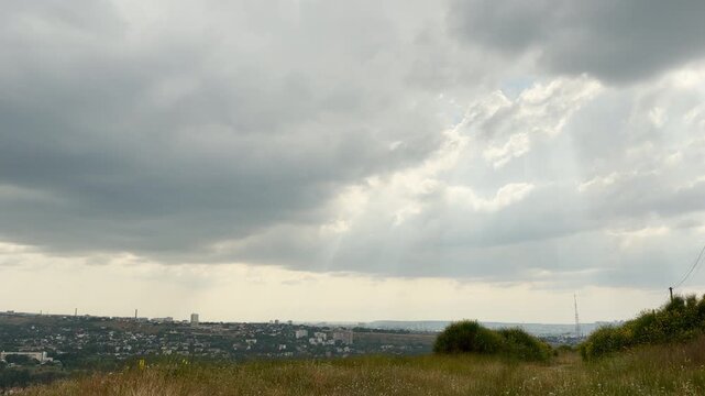 Sunbeams break through dark storm clouds over Simferopol, Crimea. Grassy hills look out over the quiet city, inspiring a hopeful feeling of awe.