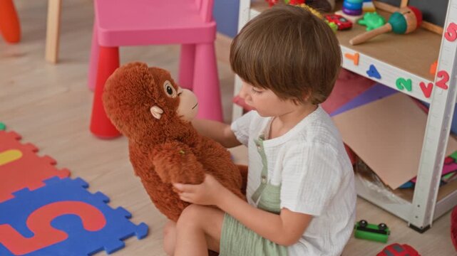 Boy sits hugging a brown stuffed monkey near toy shelf and foam number mat in a playroom; comfort playtime.