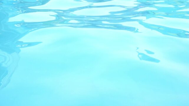 Glistening light refractions dancing on turquoise swimming pool water surface with rhythmic gentle ripples during slow motion close up camera tracking.