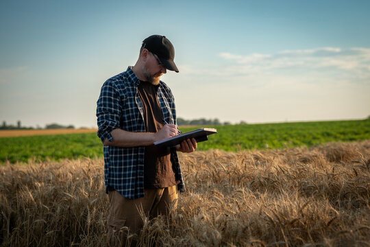 Middle aged male farmer standing in a field and writing notes on a paper clipboard