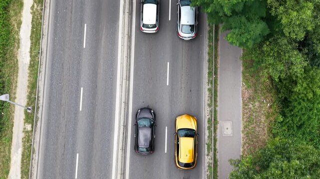 Aerial view of a traffic jam on a busy road, showcasing multiple vehicles including cars and a bus, surrounded by greenery and urban infrastructure in a vibrant setting