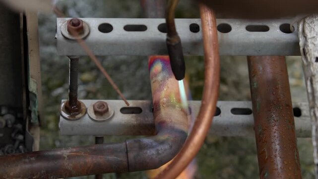 Close-up of brazing copper pipes with a gas torch with a distinctive green flame. Professional plumbing repair or HVAC air conditioning installation process, industrial soldering connection