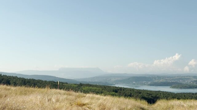Mount Chatyr-Dag stands quietly on the horizon of Simferopol, Crimea. Wide green forests and a calm reservoir rest under the clear sky, bringing a peaceful feeling of wonder.