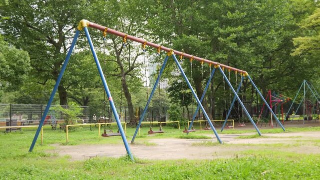Swing set swaying in urban park surrounded by trees