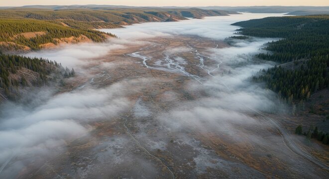 Aerial view of foggy landscape with river flowing through forest and hills