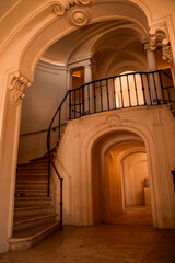 Curved ornate interior staircase with wrought iron balustrade, plaster moldings and arched doorways in a historic building hallway © PIC by Femke