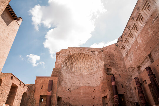 Open-air interior of ancient Roman brick ruins with large semicircular apse and vaulted walls under a bright blue sky with scattered clouds