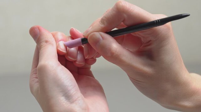 Close-up of a woman doing a DIY home manicure, gently pushing back cuticles with a ceramic stone cuticle remover tool for clean, neat natural nails.