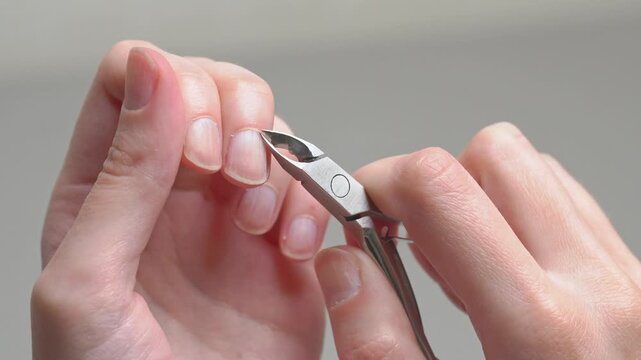 Woman cutting cuticles with professional metal nippers during a home manicure routine, focusing on precise nail care hygiene and beauty processing.