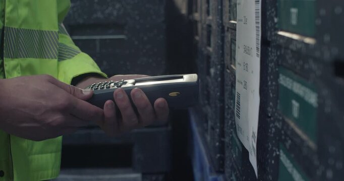 A forklift operator in a warehouse scans a barcode on a pallet of storage bins using a handheld scanner.