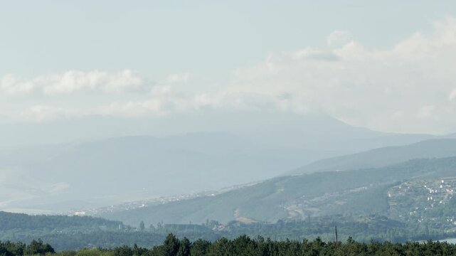 Mount Chatyr-Dag stands majestically beyond the misty hills of Simferopol, Crimea. The pale, cloudy sky evokes a deeply peaceful and nostalgic feeling.