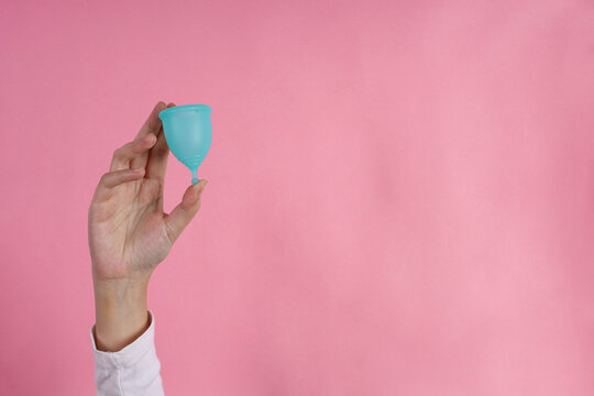 Adult Female Hand Holds Silicone Menstrual Cup Against Pink Background