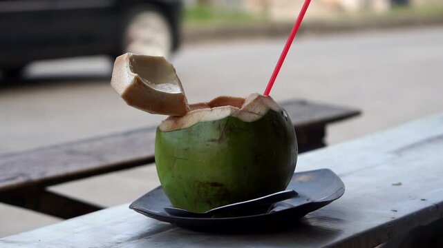 Fresh young coconut ready to drink, served with a red straw.	