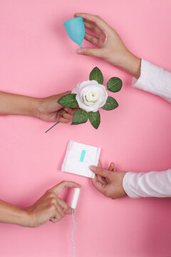 Four Hands Reach Into The Frame Holding Menstrual Cup Rose Sanitary Pad