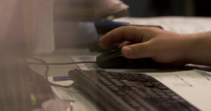 A close-up view of a hand operating a black computer mouse on a desk within an office workspace.