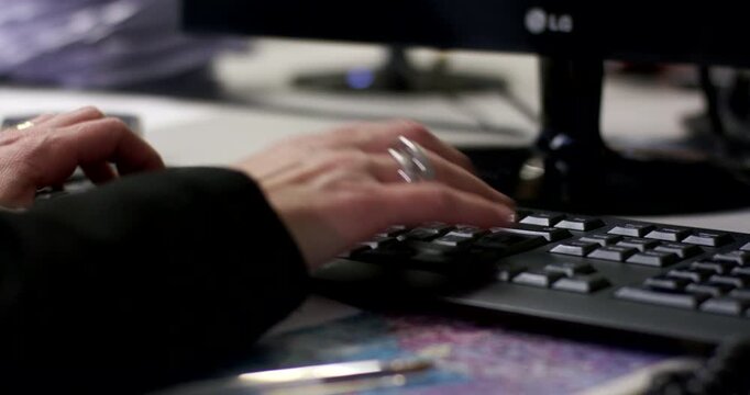 Close-up of a person's hands typing on a standard computer keyboard at an office desk.