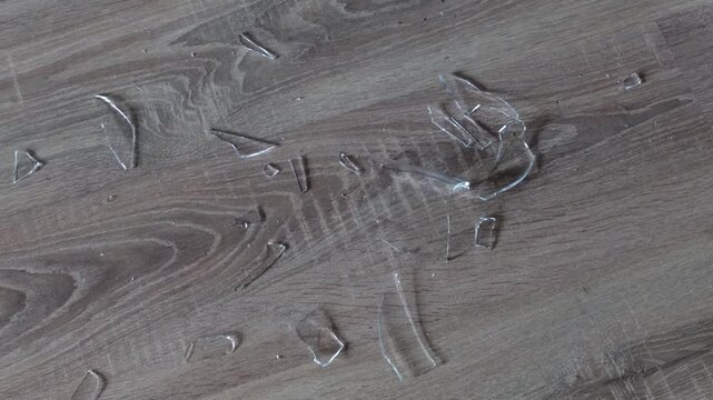 Bare hand picking up sharp broken glass shards from a wooden floor