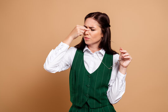 Business woman pinching her nose in disgust while holding glasses, tired and frustrated with a bad smell or headache in a studio portrait