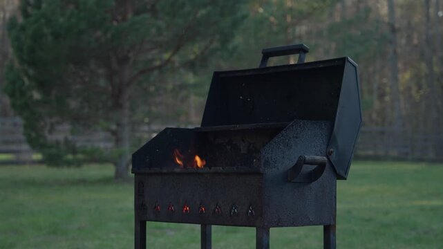 Outdoor charcoal grill smoking in a backyard garden near a house