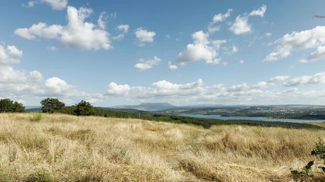 Mount Chatyr-Dag rises under a bright cloudy sky over the golden fields and reservoir in Simferopol, Crimea. This magnificent view brings a joyful and deeply peaceful feeling.