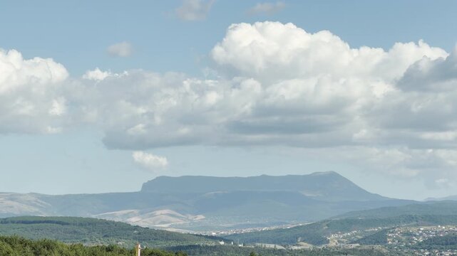 Mount Chatyr-Dag stands majestically on the horizon of Simferopol, Crimea. Massive white clouds float above the rolling green hills, bringing a powerful feeling of peaceful awe.
