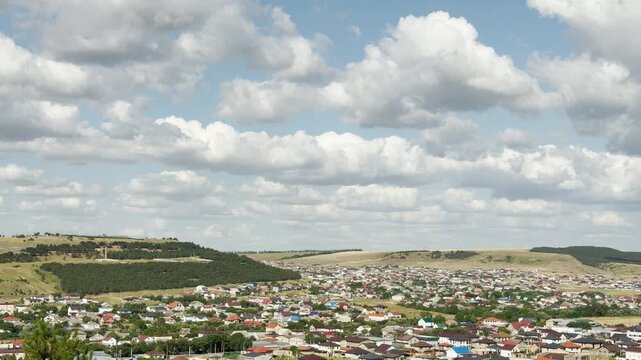 Many colorful suburban houses spread across rolling green hills in Crimea. Fluffy white clouds fill the wide blue sky, bringing a joyful and peaceful feeling of happy freedom.