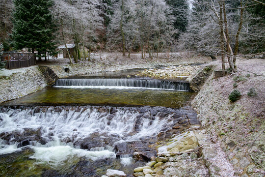 Mountain river with stepped concrete weirs surrounded by frosted winter forest
