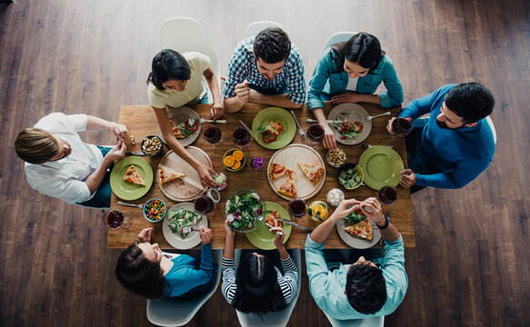 Friends gathered around a wooden table sharing pizza, salad and wine during a casual dinner party and conversation