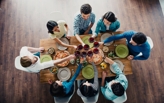 Friends toasting with red wine around a dining table with pizza and salad &mdash; casual dinner gathering and cheerful celebration among young adults